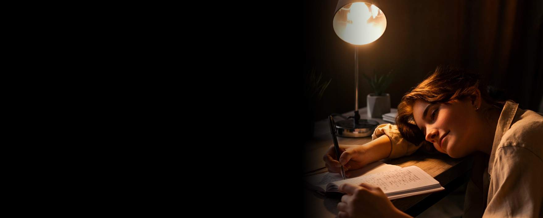 Perempuan menulis di jurnal, ditemani cahaya hangat lampu meja